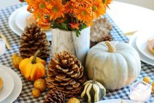 a beautiful modern woodland Thanksgiving tablescape with a plaid runner, pinecones, gourds and bright blooms plus layered plates