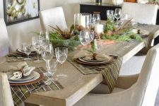 a beautiful natural-colored woodland Thanksgiving tablescape with a tray with pinecones, evergreens, candles, plaid placemats and a woven charger