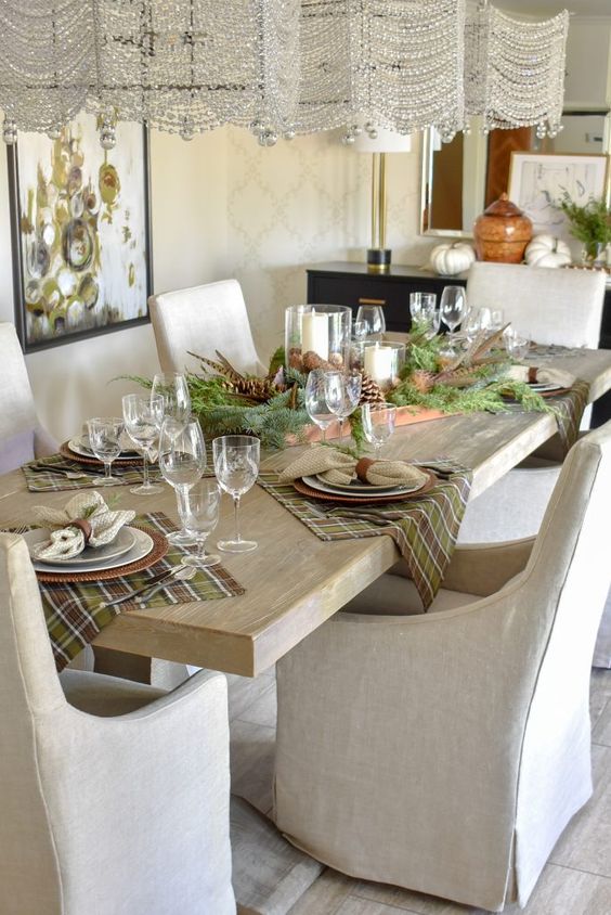 a beautiful natural-colored woodland Thanksgiving tablescape with a tray with pinecones, evergreens, candles, plaid placemats and a woven charger