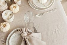 a beautiful white and off-white Thanksgiving tablescape with white pumpkins, candles, dried grasses, speckled plates and neutral linens