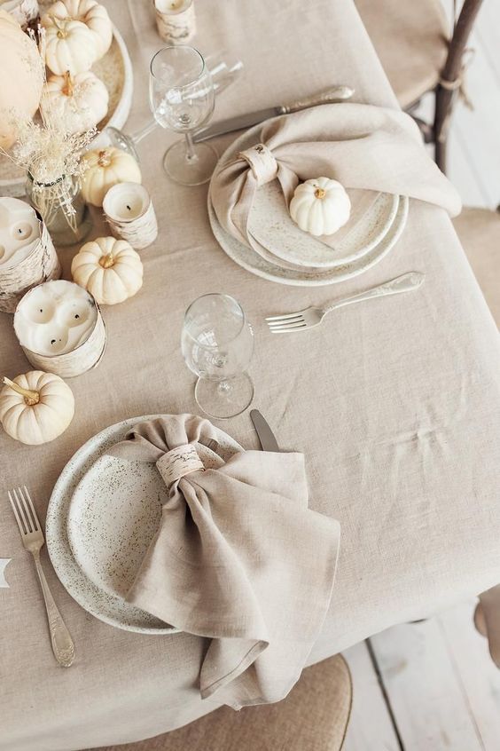 a beautiful white and off white Thanksgiving tablescape with white pumpkins, candles, dried grasses, speckled plates and neutral linens