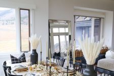 a black and white Thanksgiving tablescape with black vases and candleholedrs, wood slice placemats and white pumpkisn