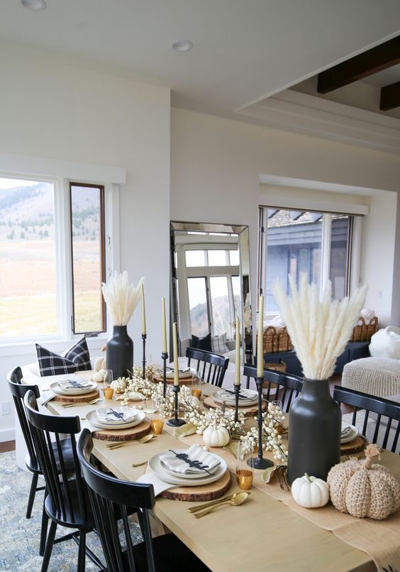 a black and white Thanksgiving tablescape with black vases and candleholedrs, wood slice placemats and white pumpkisn