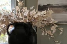 a black vase with white dried leaves, a white bowl with mini pumpkins as Thanksgiving decor