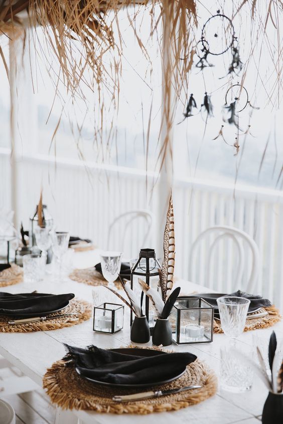 a boho black and white Thanksgiving tablescape with woven placemats, black porcelain and feathers, candles