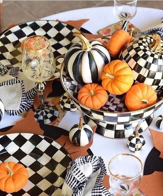a bold Thanksgiving tablescape done in black and white, with printed pumpkins and checked tableware, spruced up with orange pumpkins