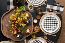 a bold black and white Thanksgiving table setting with a black table, buffalo check linens and plates, a moody floral centerpiece and copper cutlery