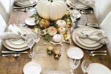 a chic Thanksgiving table with a burlap runner, white porcelain, white pumpkins, antlers, lights and greenery looks stylish