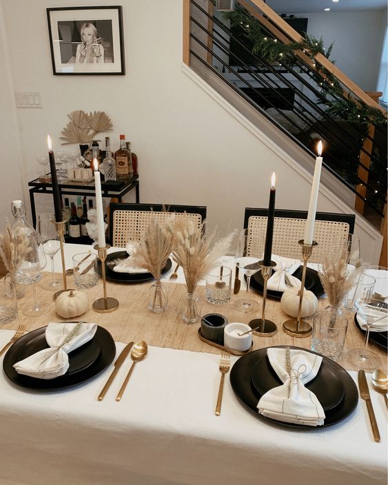 a chic black and white Thanksgiving table setting with black porcelain, black and white candles, white linens and dried grasses