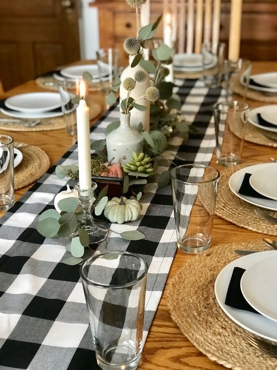 a chic rustic Thanksgiving tablescape with a plaid runner, green and white pumpkins, candles, aillum arrangements and black napkins