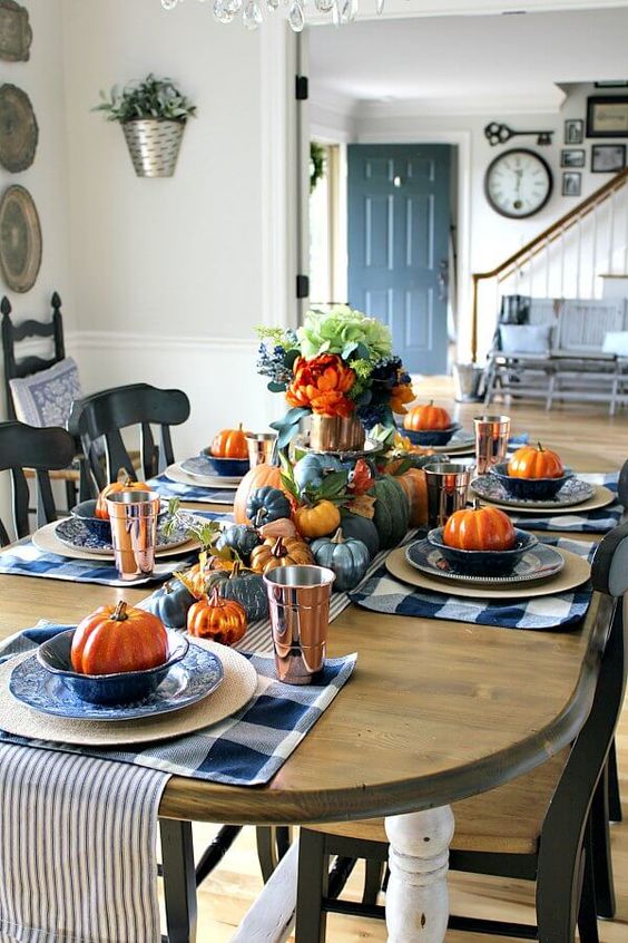 a colorful Thanksgiving tablescape with blue buffalo check placemats, bold faux pumpkins, bright blooms and tall copper glasses