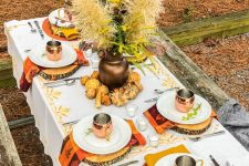 a cool forest Thanksgiving tablescape with orange placemats, wood slices, bold napkins, a grass and foliage centerpiece and copper mugs