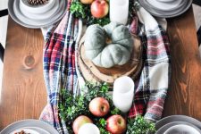 a cozy and lovely woodland Thanksgiving table setting with a plaid runner, apples and greenery, pillar candles and heirloom pumpkins, large pinecones