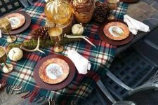 a cozy woodland Thanksgiving tablescape with a plaid table runner, moss, antlers, pinecones, metal chargers and cool plates plus fall leaves