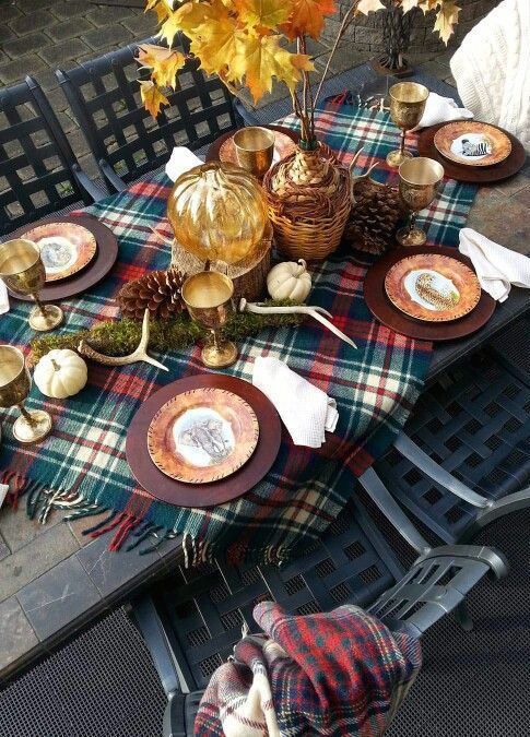 a cozy woodland Thanksgiving tablescape with a plaid tablecloth, large pinecones, antlers, bold leaves and pumpkins plus dark chargers
