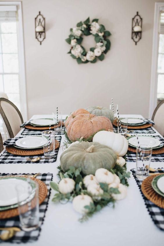 a farmhouse Thanksgiving tablescape with buffalo check placemats, natural pumpkins and greenery, woven placemats
