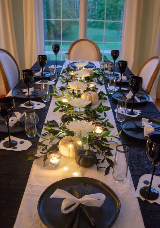 a glam black and white Thanksgiving tablescape with a white runner, black glasses, black and white pumpkins, black plates and white blooms