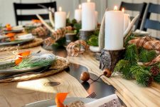 a gorgeous woodland Thanksgiving table with woven placemats, speckled plates, evergreens, pinecones, antlers and tree branch candleholders