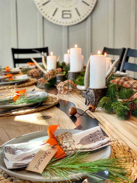 a gorgeous woodland Thanksgiving table with woven placemats, speckled plates, evergreens, pinecones, antlers and tree branch candleholders
