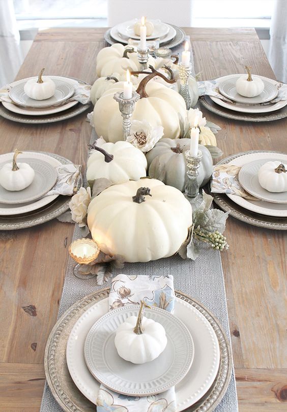a grey and white Thanksgiving tablescape with a grey runner, white and grey pumpkins, blooms, candles and white pumpkins