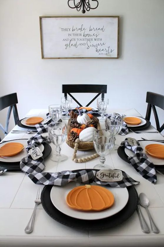 a lovely Thanksgiving tablescape in black and white, with ornage pumpkin plates, beads, a centerpiece of pinecones and pumpkins