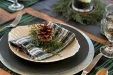 a lovely and simple woodland tablescape with plaid placemats, black plates, pinecones and evergreens, candles is great for Thanksgiving and Christmas