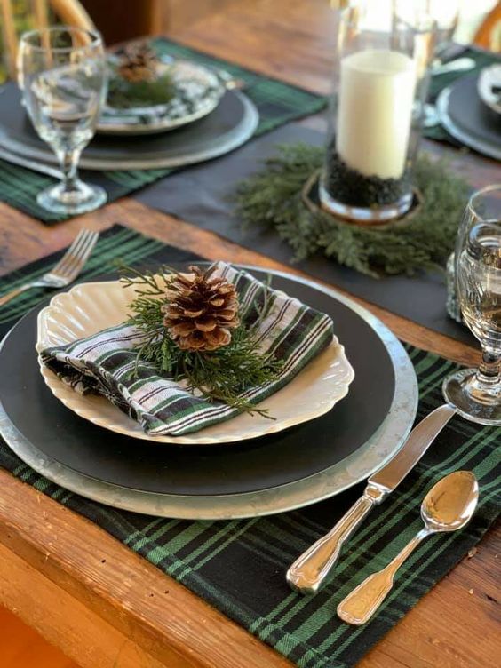 a lovely and simple woodland tablescape with plaid placemats, black plates, pinecones and evergreens, candles is great for Thanksgiving and Christmas