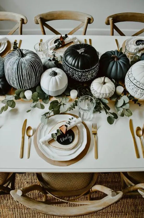a lovely black and white boho Thanksgiving tablescape with folk painted pumpkins, greenery, candles, chargers, gold cutlery