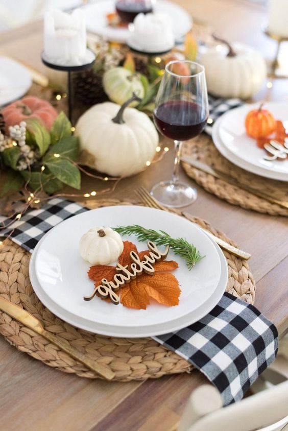 a lovely modern famrhouse Thanksgiving tablescape with woven chargers, buffalo check napkins, lights, pumpkins and leaves
