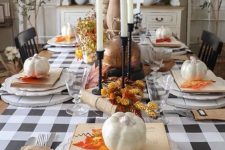 a lovely vintage Thanksgiving tablescape with buffalo check linens, tall candles, pinecones, faux pumpkins and faux bright leaves
