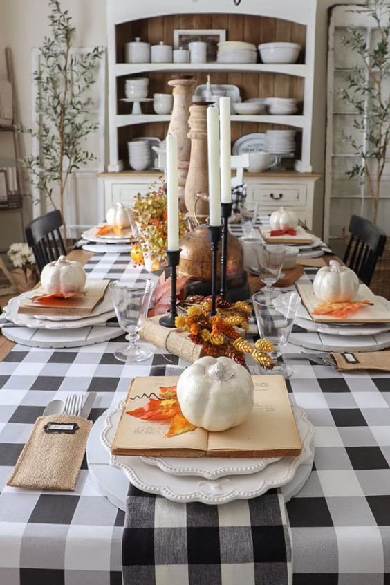 a lovely vintage Thanksgiving tablescape with buffalo check linens, tall candles, pinecones, faux pumpkins and faux bright leaves
