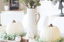 a lovely white Thanksgiving table runner of fabric, greeneyr, small and large white pumpkins and greenery in a jug