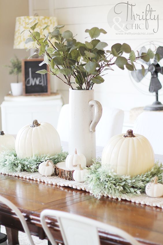 a lovely white Thanksgiving table runner of fabric, greeneyr, small and large white pumpkins and greenery in a jug