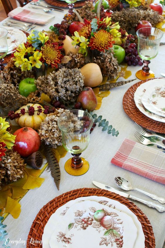 a lush rustic to woodland Thanksgiving centerpiece of lotus, pomegranates, pumpkins, pears, apples, feathers, bold blooms and dried hydrangeas