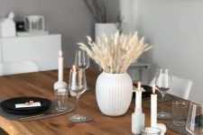 a minimalist monochromatic Thanksgiving tablescape with black plates, grey placemats, candles and bunny tails in a vase