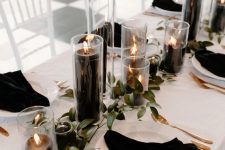 a modern black and white Thanksgiving tablescape with black pillar candles, white porcelain and black napkins and greenery