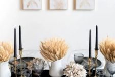 a modern glam Thanksgiving tablescape with wheat in vases, black candles and plates, a black runner and gold cutlery