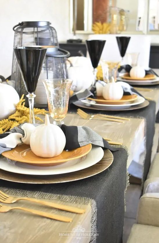 a modern rustic Thanksgiving tablescape with black placemats and striped napkins, gold chargers and plates, gold cutlery, black glasses and candle lanterns