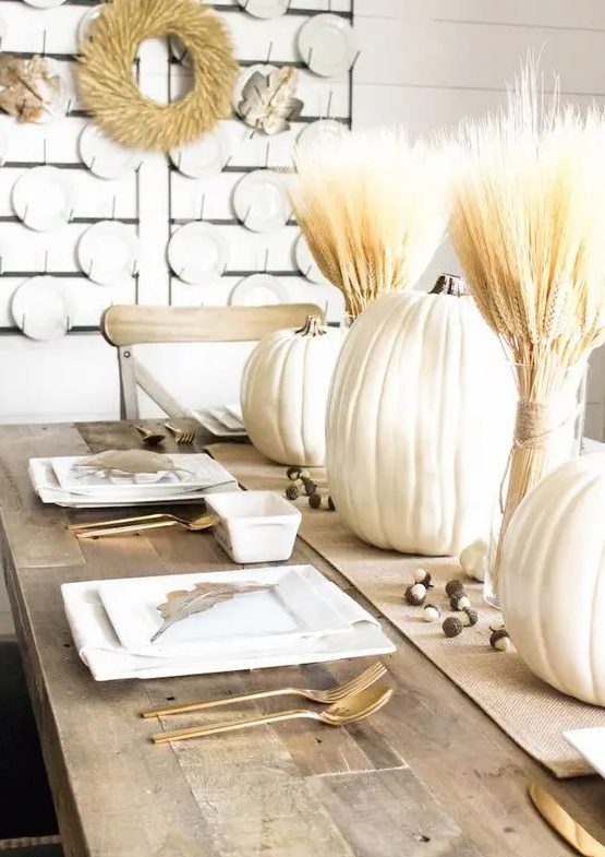 a natural white Thanksgiving tablescape with a burlap runner, wheat, pumpkins, square plates, gold cutlery