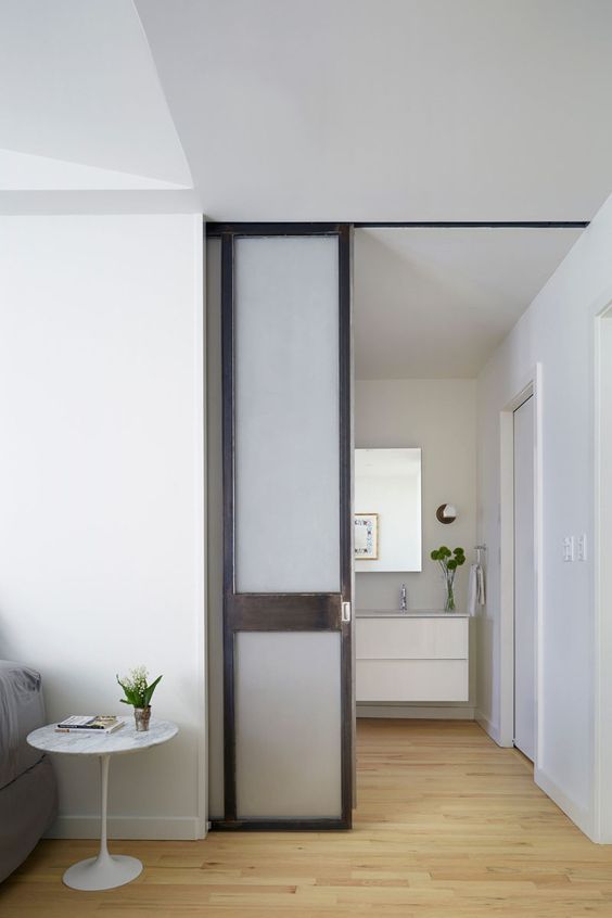 a neutral contemporary space with minimalist and sleek furniture and with matching white frosted glass pocket doors that hide an en suite bathroom