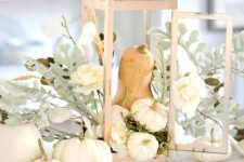 a pretty Thanksgiving centerpiece of a candle lantern with a gourd and mini white pumpkins, greenery and white blooms