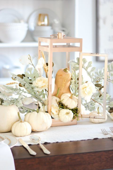 a pretty Thanksgiving centerpiece of a candle lantern with a gourd and mini white pumpkins, greenery and white blooms