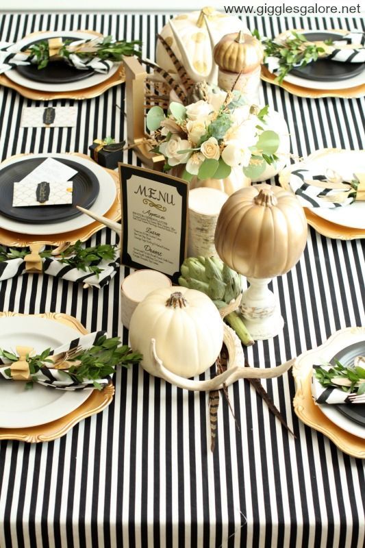 a pretty Thanksgiving tablescape with a striped tablecloth, black and white plates, gold chargers, white and gold pumpkins and antlers