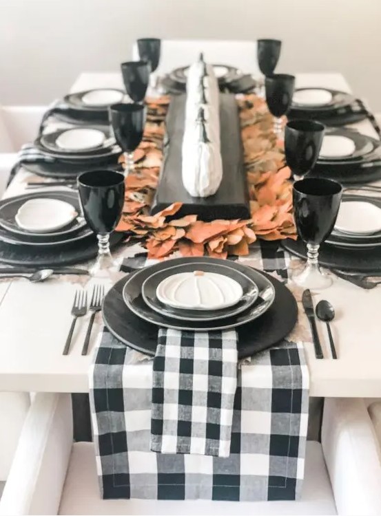 a pretty modern rustic Thanksgiving tablescape with black plates, buffalo check linens, fall leaves, small white pumpkins