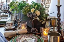 a refined Thanksgiving tablescape with a wooden box centerpiece with snowy pinecones, greenery and artichokes, refined green printed plates and goblets