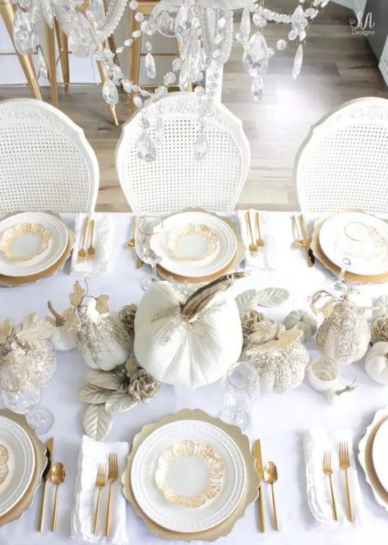 a refined Thanksgiving tablescape with gold chargers, cutlery, white glitter pumpkins and metallic leaves