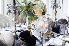 a refined and chic black adn white Thanksgiving table with grey, black and white velvet pumpkins, black candles in crystal candleholders, blooms and refined plates