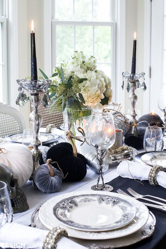 a refined and chic black adn white Thanksgiving table with grey, black and white velvet pumpkins, black candles in crystal candleholders, blooms and refined plates