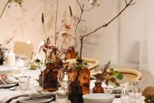 a refined contemporary nature-inspired Thanksgiving tablescape with neutral linens, branches and twigs, foliage and amber glass bottles