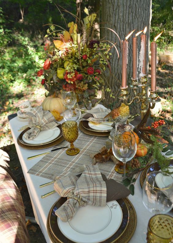 a refined vintage forest Thanksgiving tablescape with plaid linens, various porcelain, copper candles, feathers, bold blooms, pinecones and feathers